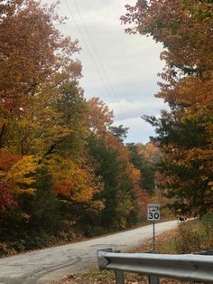 an empty road surrounded by trees with fall foliage on the sides and a speed limit sign in the foreground