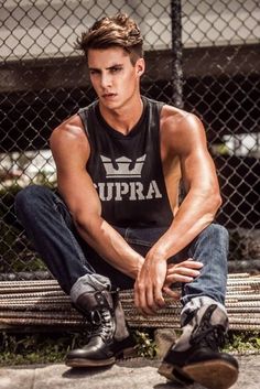 a young man sitting on top of a wooden bench next to a chain link fence