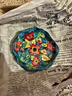 a blue bowl with flowers painted on it sitting on top of a piece of newspaper