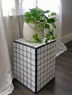 a potted plant sitting on top of a white and black tiled box next to a window