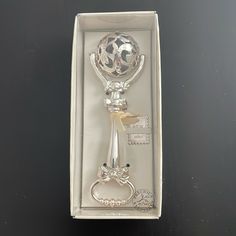 a silver bottle opener in a white box on a table with a keychain