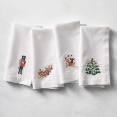 four embroidered christmas napkins on a white surface with an image of santa claus, nutcracker and tree