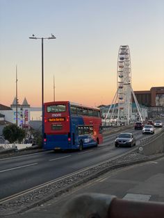 a red and blue double decker bus driving down a street next to a ferris wheel