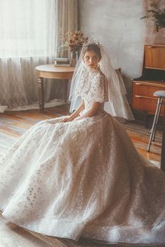 a woman in a wedding dress sitting on the floor next to a piano and window