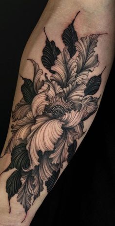 a black and white flower tattoo on the left arm, with leaves in the center