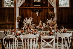 the table is set with white chairs and floral centerpieces on top of it