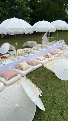 an outdoor table set up with umbrellas and flowers on the grass for a wedding reception