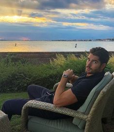 a man sitting on top of a chair in front of a body of water at sunset