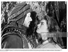 the man and woman are standing next to each other in front of a rock wall