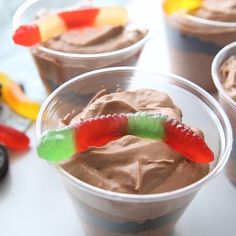 three cups with chocolate pudding and candy worms in them on a table next to halloween candies