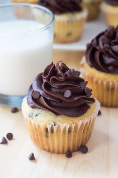 two cupcakes with chocolate frosting and chocolate chips next to a glass of milk