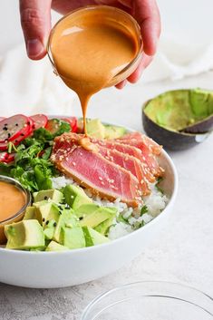 someone pouring dressing on a salad with avocado and other foodstuffs in the background