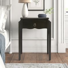 a black table with a lamp on top of it next to a bed and a painting