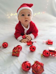 a baby wearing a santa claus outfit surrounded by christmas ornaments