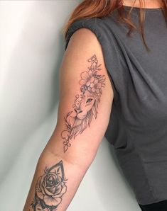 a woman's arm with flowers and a mask tattoo on her left arm, next to a white wall