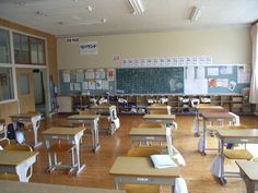 an empty classroom filled with desks and chairs next to a chalkboard on the wall