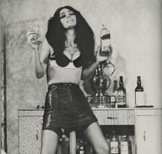 a black and white photo of a woman holding a glass in her hand while sitting on a stool