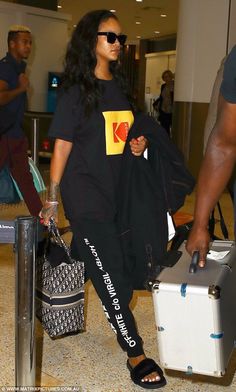 a woman in black shirt and leggings carrying luggage at an airport with other people