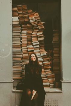 a woman sitting on a bench in front of a large stack of book's