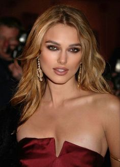 a woman in a red dress with long hair and large earrings on her head, posing for the camera