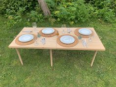 a wooden table with plates and glasses on it in the grass next to some trees