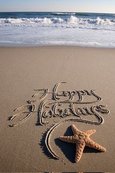 happy holidays written in the sand with a starfish on the beach next to it