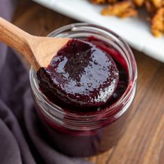 a jar filled with blueberry jam on top of a wooden spoon next to some fried food