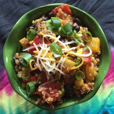 a green bowl filled with lots of food on top of a colorful table cloth next to a fork