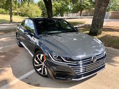 a gray volkswagen sedan parked in a parking lot next to some trees and grass on a sunny day