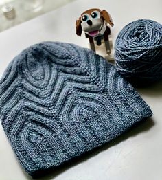 a knitted hat and ball of yarn with a dog figurine next to it