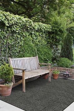 a wooden bench sitting on top of a black rug next to potted plants and trees