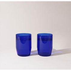 two blue glasses sitting next to each other on a white surface with the light shining through them