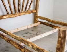 a wooden bed frame made out of logs and concrete flooring with white walls in the background