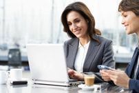 two people sitting at a table looking at a laptop