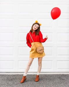 a woman in winnie the pooh costume holding a red balloon while standing next to a garage door