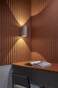 a desk with a book on it next to a lamp and chair in the corner