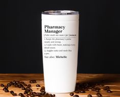 a white coffee cup sitting on top of a wooden table filled with coffee beans and the words pharmacy manager