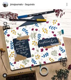 an open notebook with writing on it next to some flowers and other items that include pens