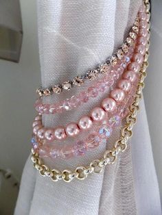 pink pearls and gold chains are attached to the curtain in front of a white drapes