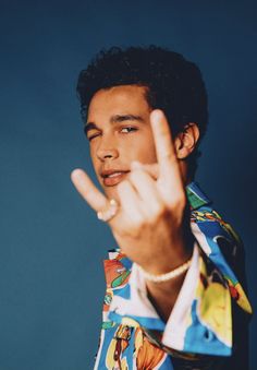 a young man making the vulcan sign with his hand while wearing a colorful shirt against a blue background