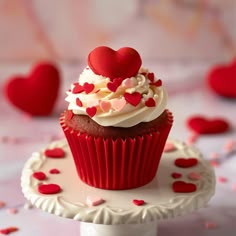 there is a cupcake with white frosting and red hearts on the cake stand