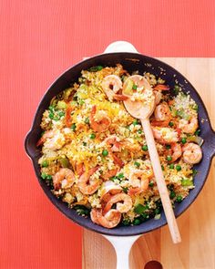 a skillet filled with shrimp and rice on top of a wooden table next to a red wall