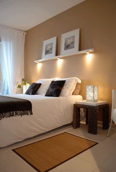 a bed sitting in a bedroom next to a window with white curtains and two framed pictures on the wall