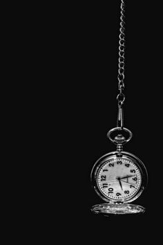 a black and white photo of an alarm clock hanging from a chain on a dark background