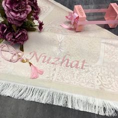 a pink and white table cloth with tassels on it next to a bouquet of flowers