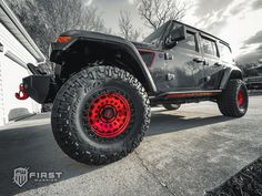 a gray and red jeep parked in front of a garage with its wheels on the ground