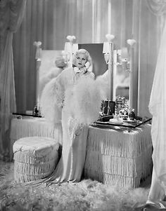 an old photo of a woman standing in front of a mirror with feathers on it