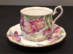 a cup and saucer with flowers painted on the side sitting on a black surface