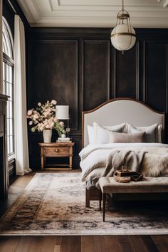 a bedroom with dark wood paneling, white bedding and flowers on the nightstand