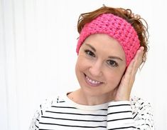 a woman wearing a pink headband smiles while holding her hand to her face and looking at the camera